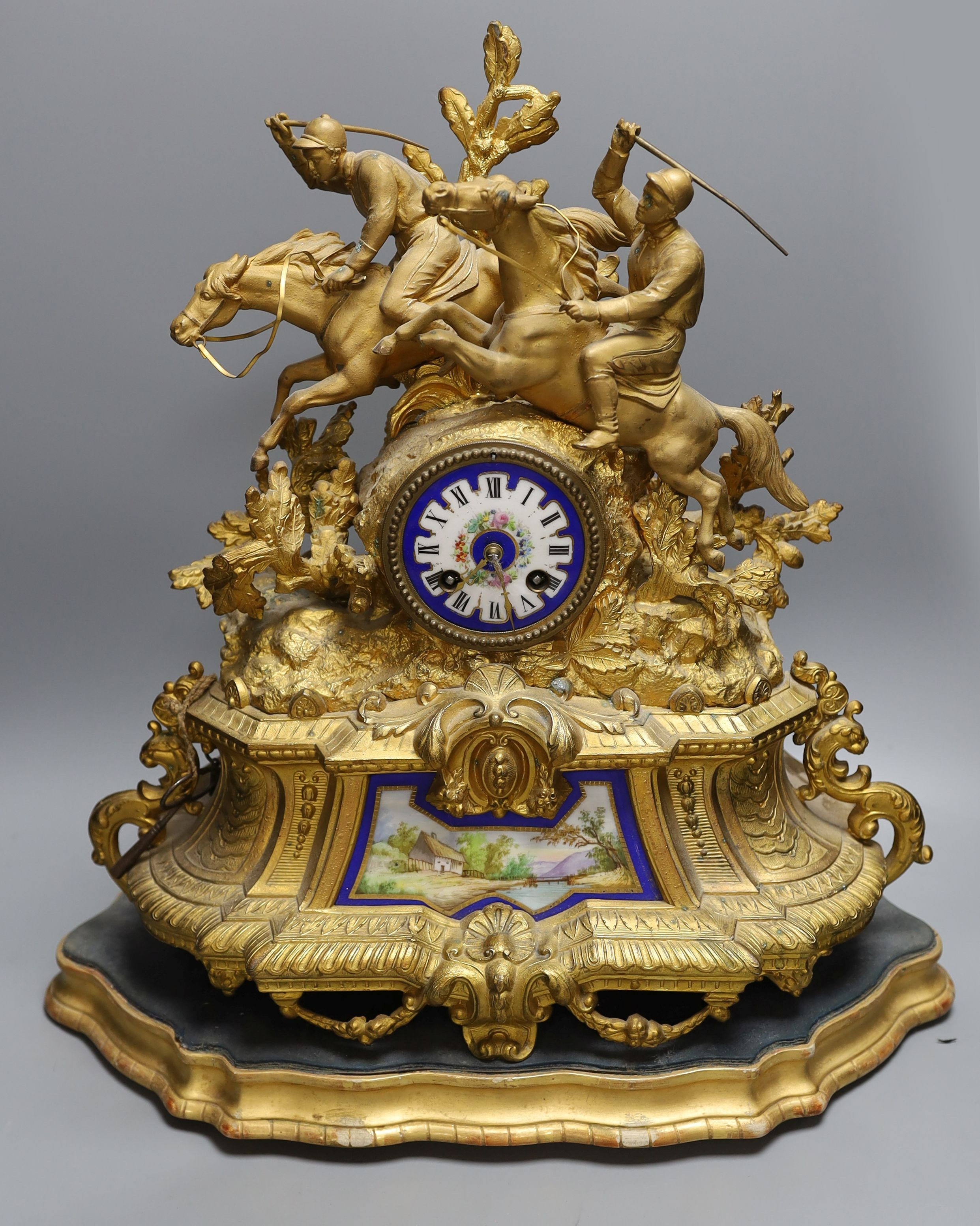 A 19th century gilt spelter mantel clock, having horse and jockey surmount with porcelain panels and circular porcelain dial, on shaped plinth base. 47cm